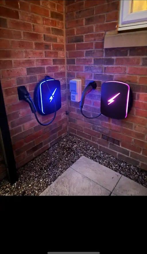 Two EV chargers fitted on a brick wall with blue and pink LED bolts and an isolator switch