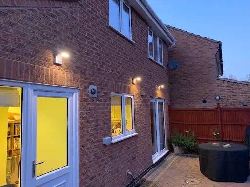 House exterior at dusk with a box wall light, downlights and lit windows