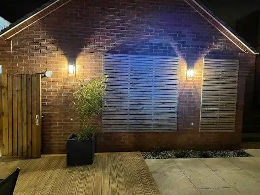 Brick house lit at night with wall lights and a soffit lighting strip along the roofline