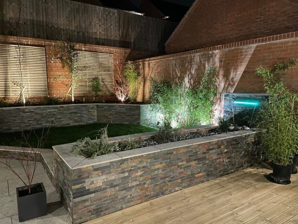 Landscaped garden lit at night with uplit fence panels, planted slate beds and a water feature
