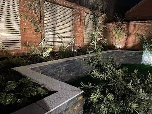 Garden at night with a slate-clad raised bed, uplit planting and spike lighting
