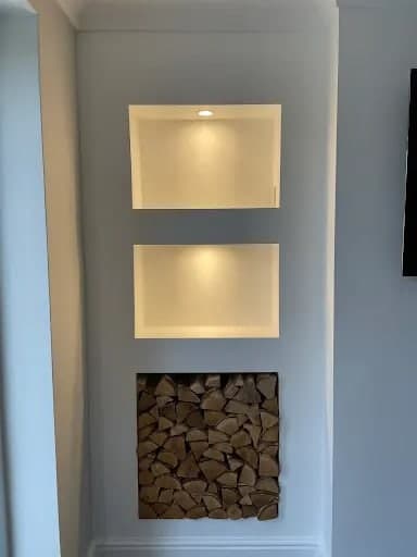 Alcove with two warm LED-lit recessed niches above a log-store feature niche